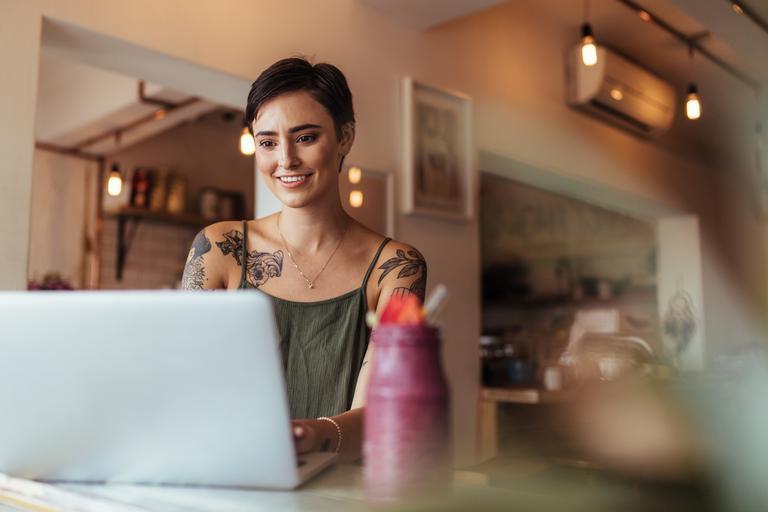 Frau mit Tattoos auf ihrem Körper arbeitet am Laptop.