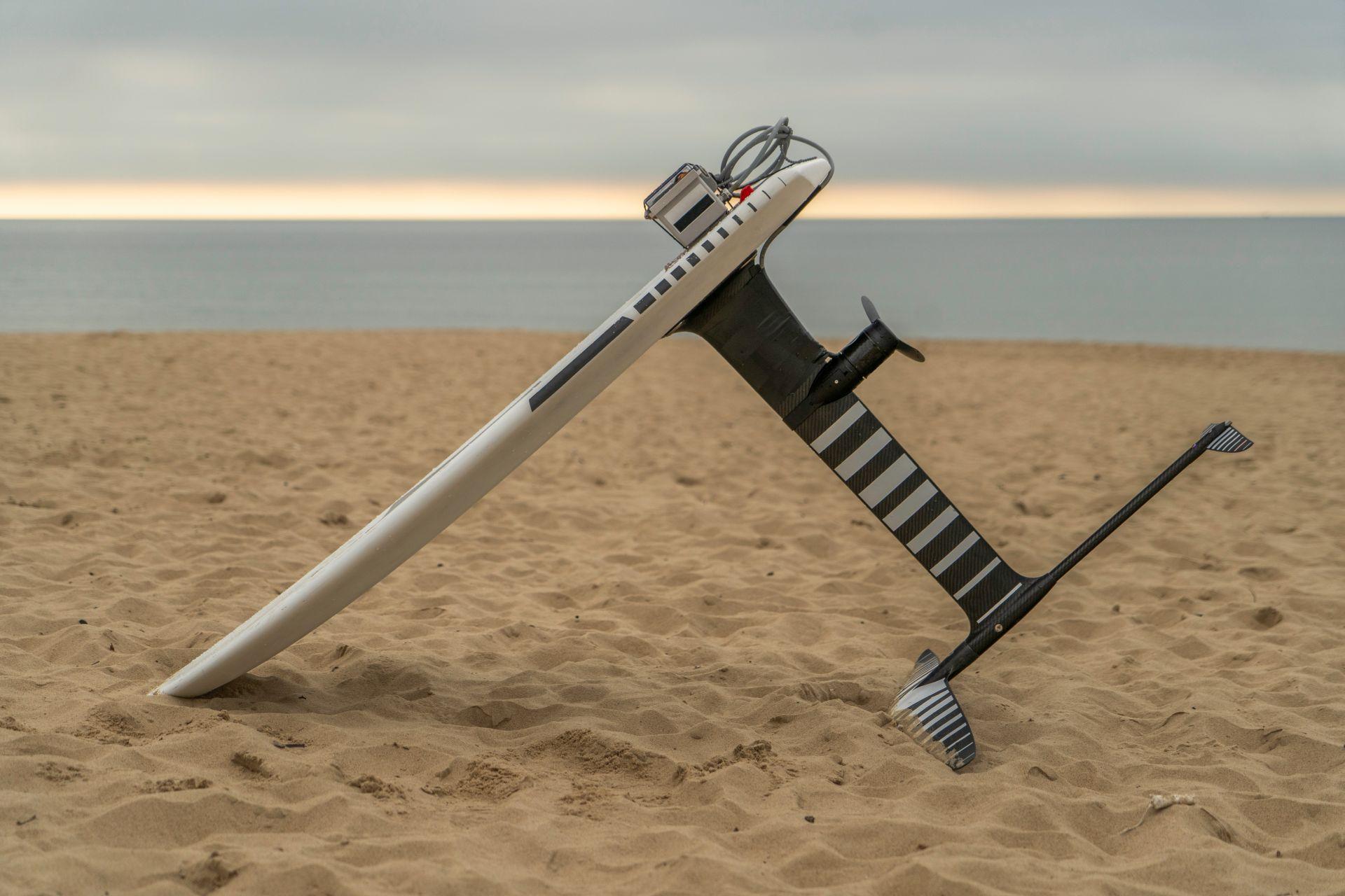 Nahaufnahme eines E-Foil-Surfboards mit Propellerantrieb am Sandstrand bei ruhiger See