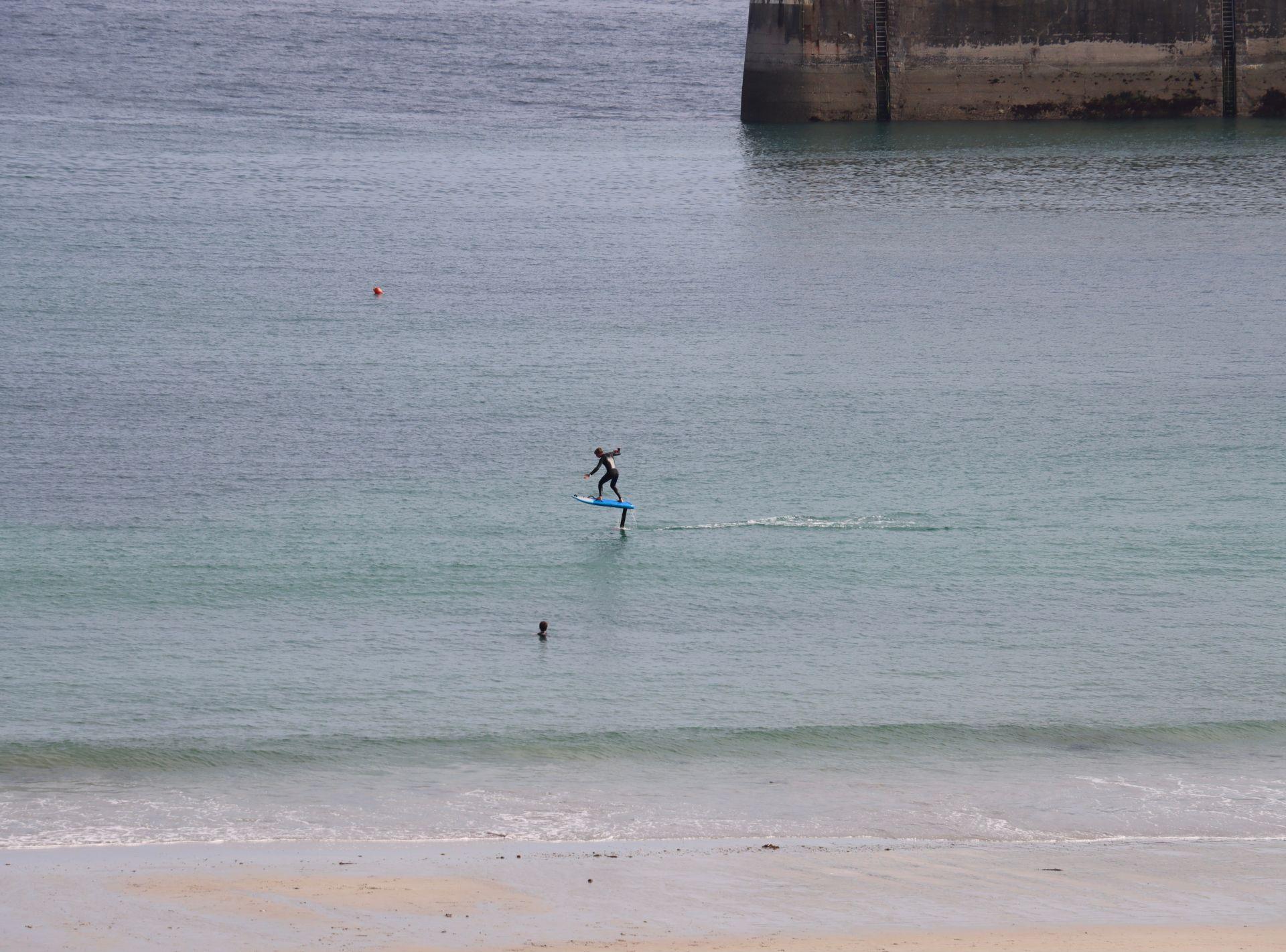 Person fährt mit elektrischem Surfboard über das Wasser nahe einer Hafenmauer
